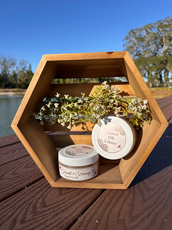 Two jars of Faith & Honey products on a wooden hexagonal tray with flowers, outdoors.